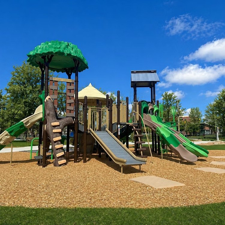 The main play structure with green tree-canopy shade and slides
